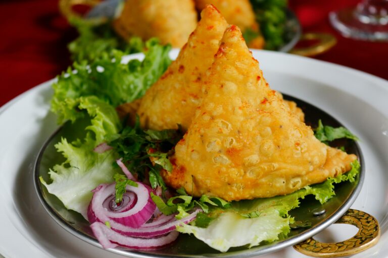 Close-up of crispy samosas served with fresh lettuce and onion rings.